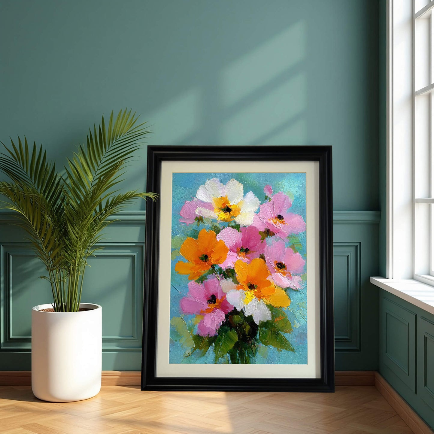A large black-framed floral painting leaning on a wooden floor against a dark teal wall with classic paneling, next to a potted palm plant.