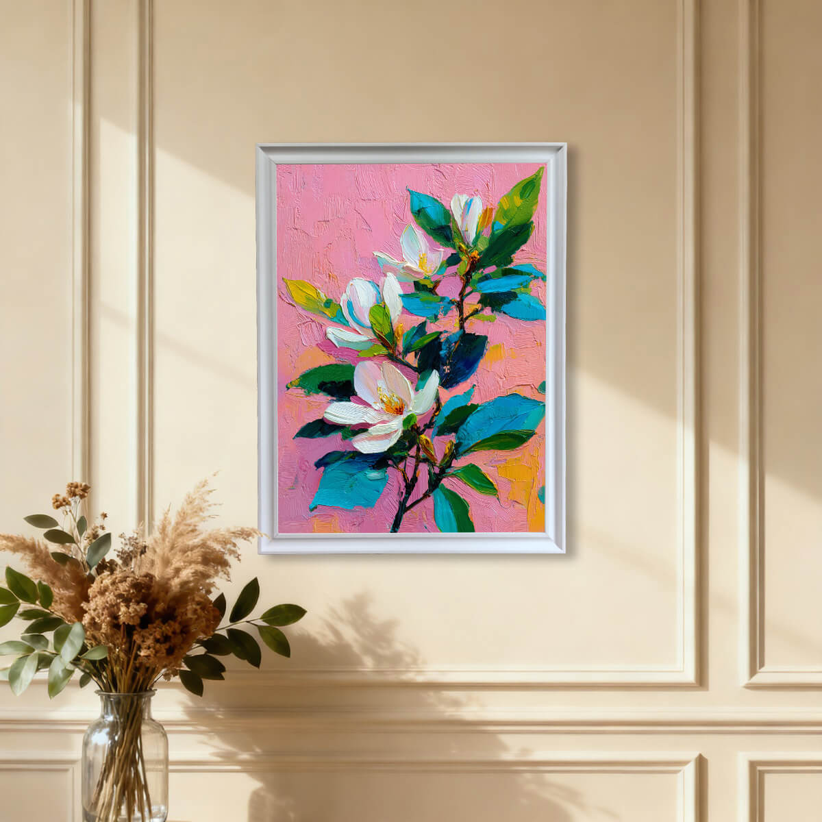 White-framed magnolia blossom print hanging on a cream-colored paneled wall near dried flowers.