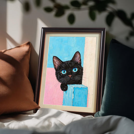 A framed print of a black cat with a coffee-colored frame rests on a bed, propped against a pillow with another pillow to the side.