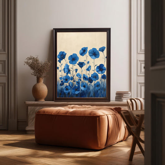 A framed art print of blue flowers with a light background. The dark brown-framed art rests on a wooden chest behind a brown ottoman and a vase with dried flowers.