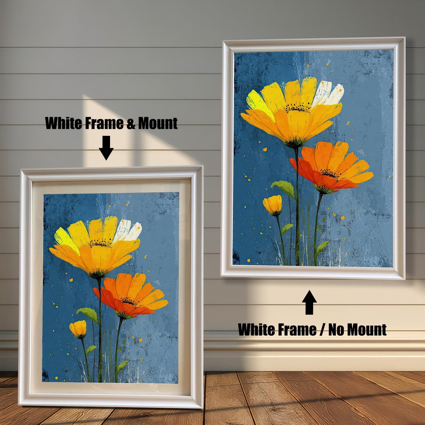 Two framed art prints of yellow and orange flowers on a wooden floor. The print on the left is in a white frame with a mount, and the one on the right is in a white frame without a mount.