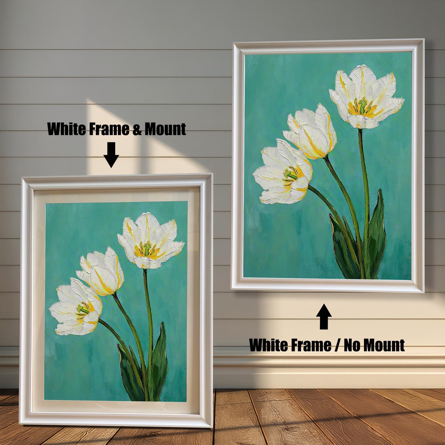 A framed art print of three white tulips. One is in a white frame with a tan mat, and the other is in the same frame without a mat. The art is against a white wooden wall.
