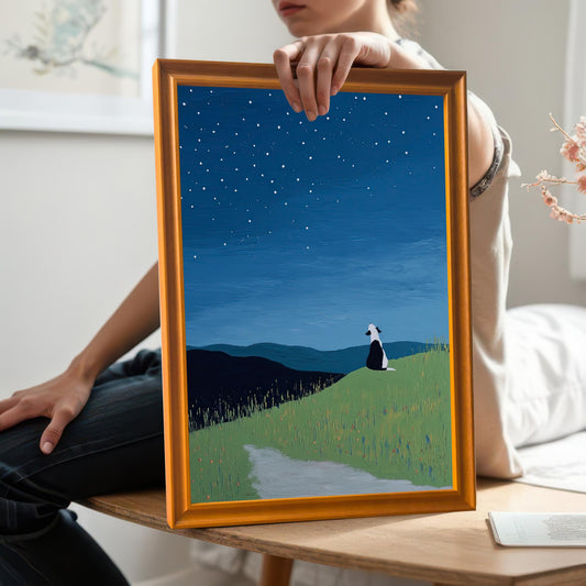 A person is holding the framed abstract dog print in a Gold/Orange frame at chest level, showcasing the artwork's scale. The person is sitting on a wooden bench, wearing a white top and dark jeans.