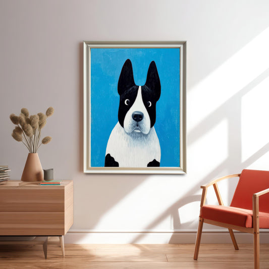 Framed painting of the black and white dog in a Light Gold/Silver frame hanging on a white wall above a wooden side table and an orange armchair, with bright sunlight shining in.