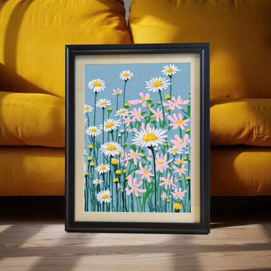 A framed art print of the daisy field illustration, set in a Black Frame with a light-colored mount, leaning on a wooden floor against a background of stacked yellow sofa cushions.