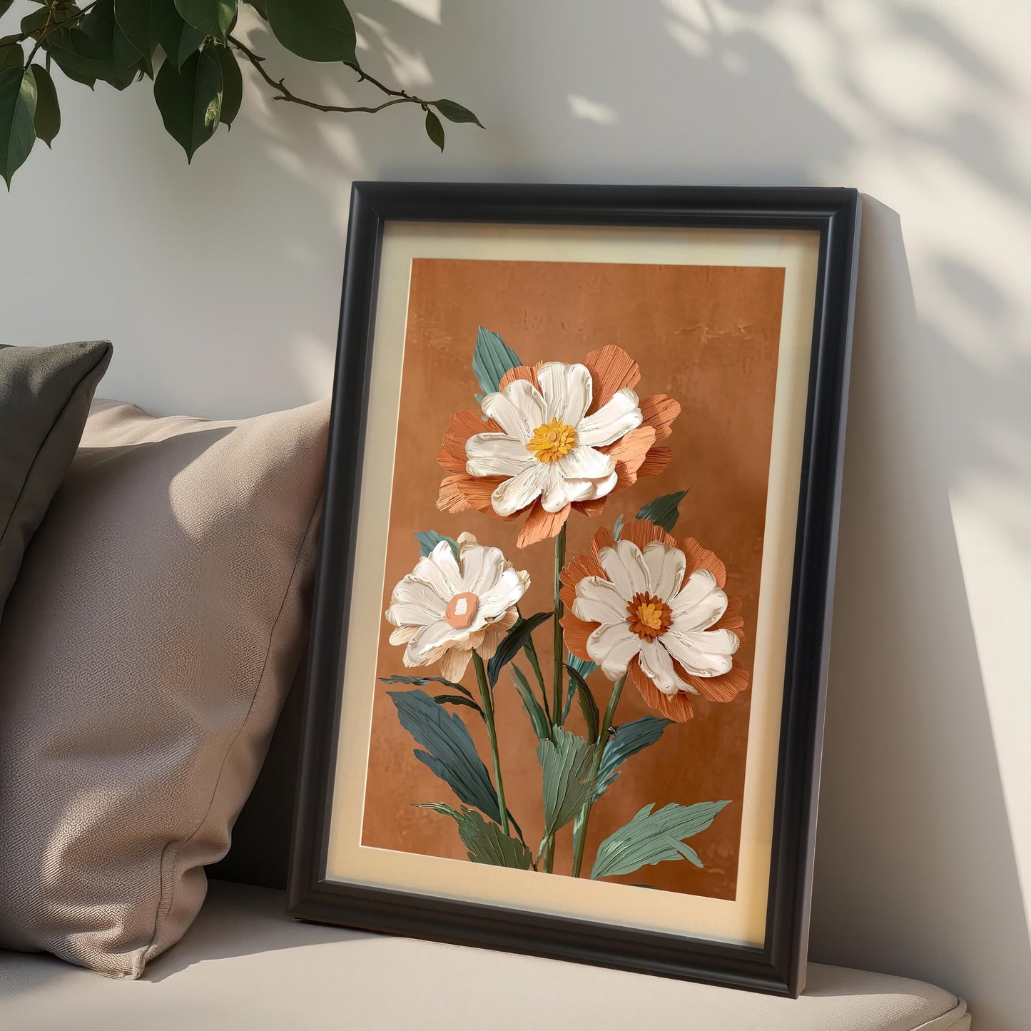 Close-up lifestyle photo of the floral art print in a Black wood frame with a mat/mount, leaning against a neutral wall with beige pillows. The print showcases an impasto-style artwork of three white and burnt-orange flowers.