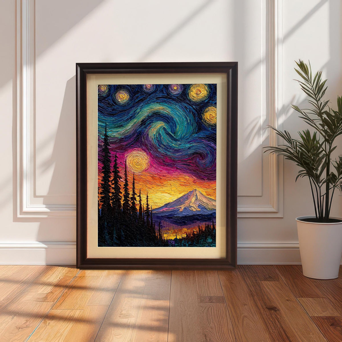 Vibrant, textured framed art print of a mountain landscape under a swirling, colorful starry night sky. The print is in a black wood frame with a mat/mount, leaning on a wooden floor against a white wainscoted wall next to a houseplant.