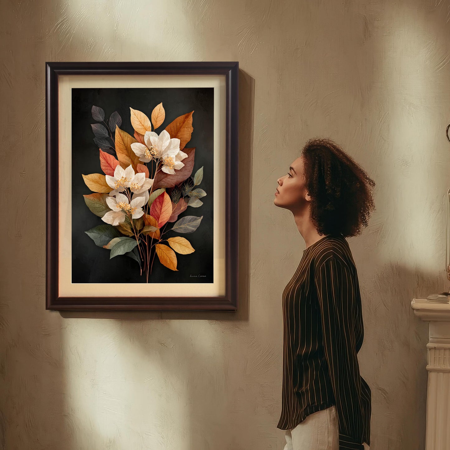 A woman with curly hair is standing and looking up admiring a framed art print of a bouquet of white flowers and autumn-toned leaves on a dark background. The art is in a dark brown (Coffee) wood frame with a mount (matting). The print hangs on a textured beige wall with dramatic shadows.
