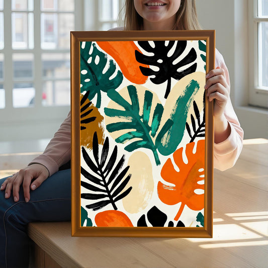 Lifestyle image of a smiling person sitting down, holding up the colorful abstract tropical leaf art print in a gold/orange wood frame to showcase the art.