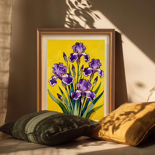 A gold-toned framed art print featuring a painting of purple Irises on yellow, propped up on a surface among dark green and yellow pillows with sunbeams and shadows falling across it.