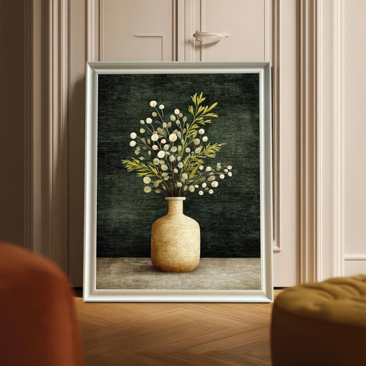 A framed art print of a vase with foliage, displayed leaning against a door with decorative molding. The frame is a White wood.