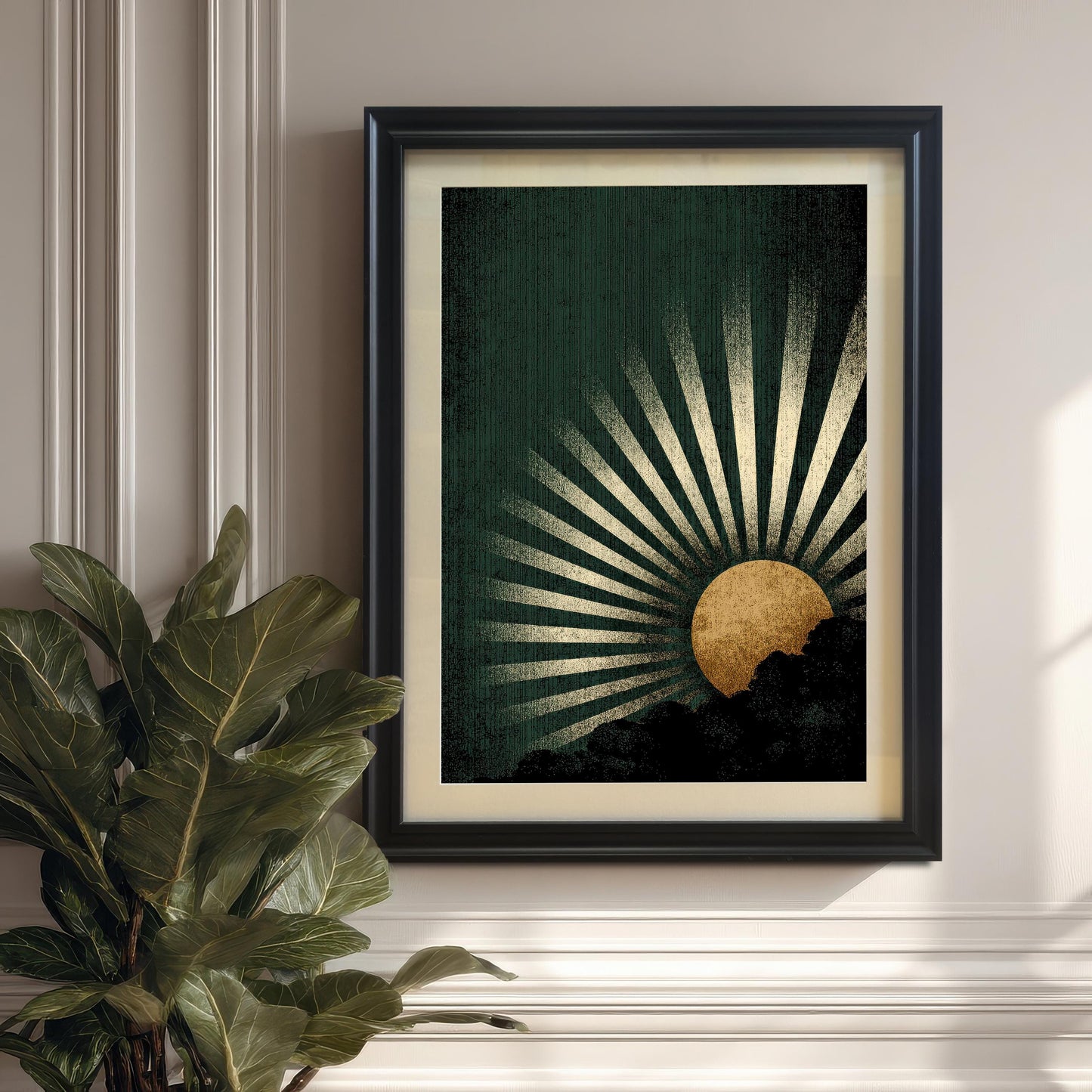 The dark green and gold sunburst art print in a Black Frame with a mount, hanging on a paneled white/cream wall. A large fiddle leaf fig plant is visible in the lower left corner.