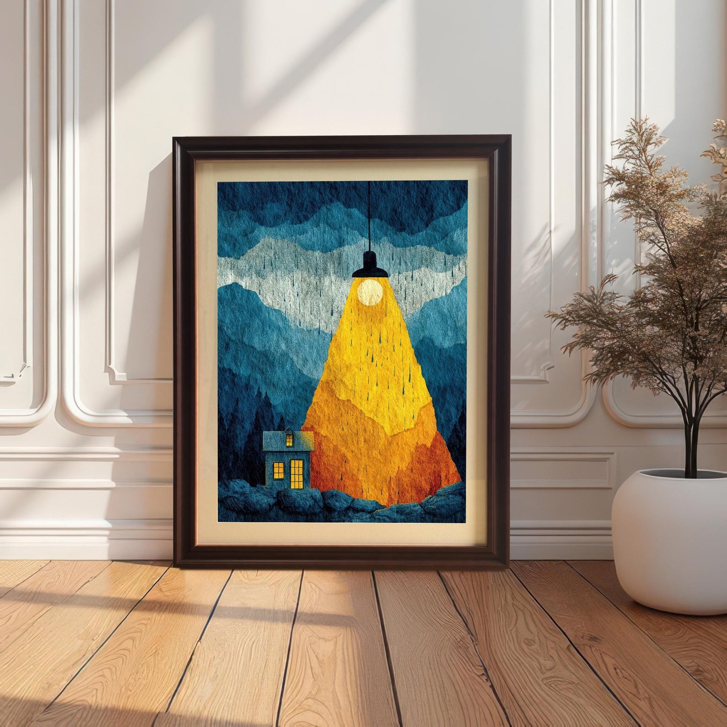 The "Spotlight House" illustration in a coffee-colored wood frame with a cream mat board, resting on a light wood floor against a decorative wainscoted wall next to a white planter.