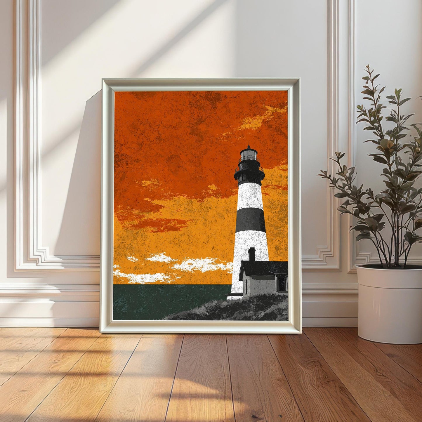 A white wood-framed lighthouse art print resting on a wooden floor in a sunlit room with elegant wall molding and a white potted plant.