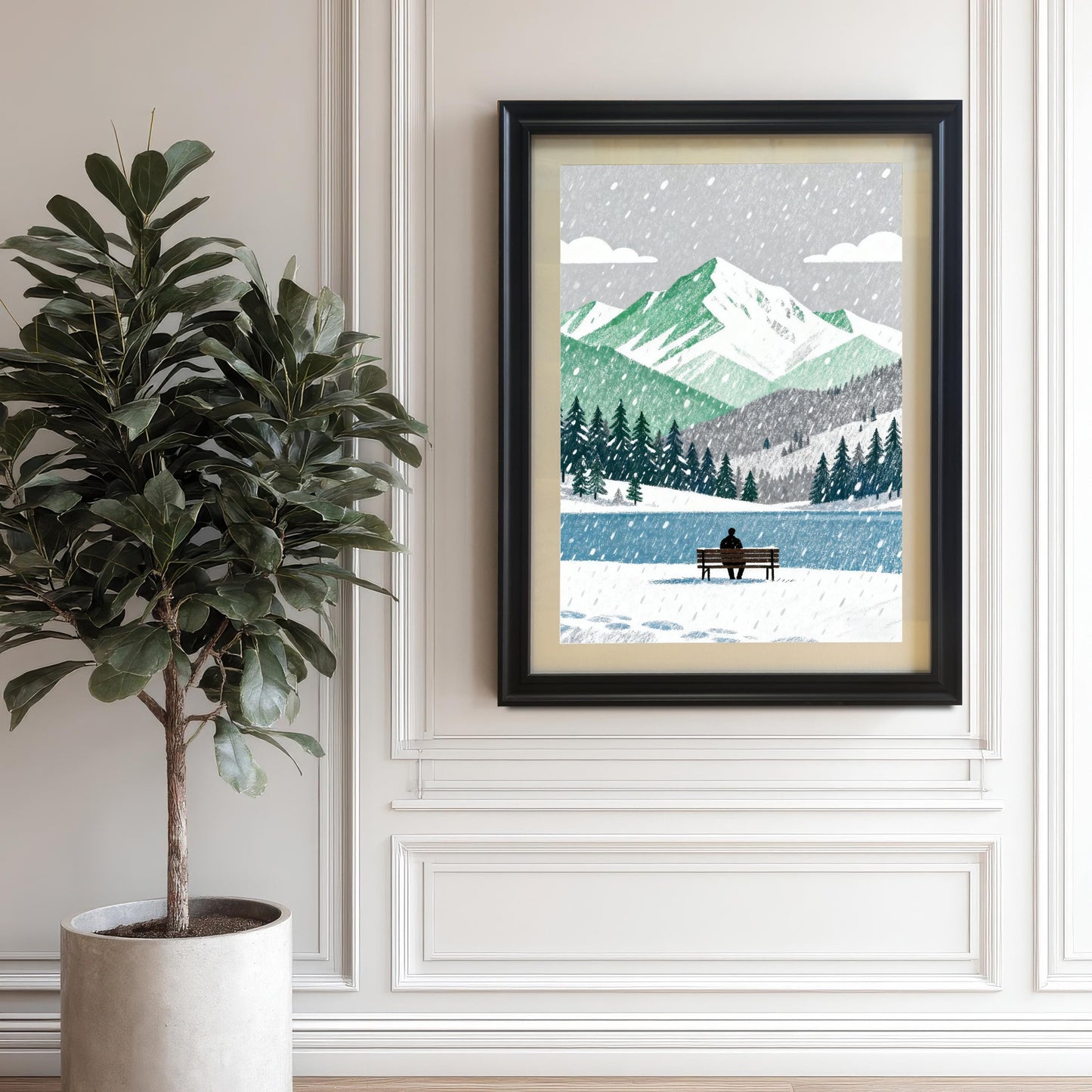 A framed art print in a black wood frame, hanging on an elegant white paneled wall next to a large potted Fiddle-leaf Fig plant. The artwork depicts a winter landscape with mountains and a person on a bench.