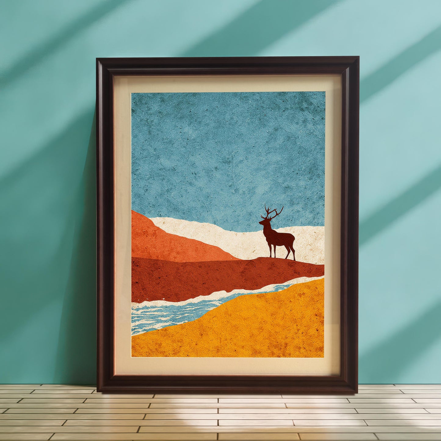 A coffee-colored wood frame with a cream mount resting on a light-colored slatted surface against a teal blue wall, accented by diagonal shadows from a nearby window.
