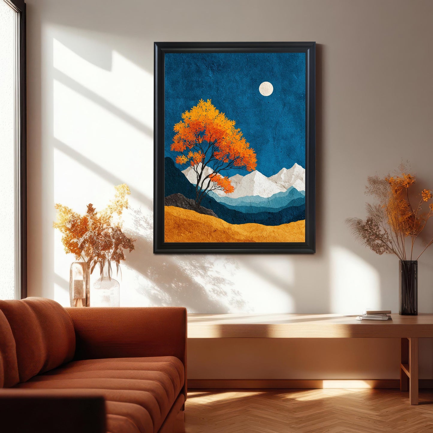A black wood framed art print featuring a vibrant orange tree and blue night sky, hung in a sunlit room over a light wood bench and terracotta-colored couch with soft shadows cast on the wall.