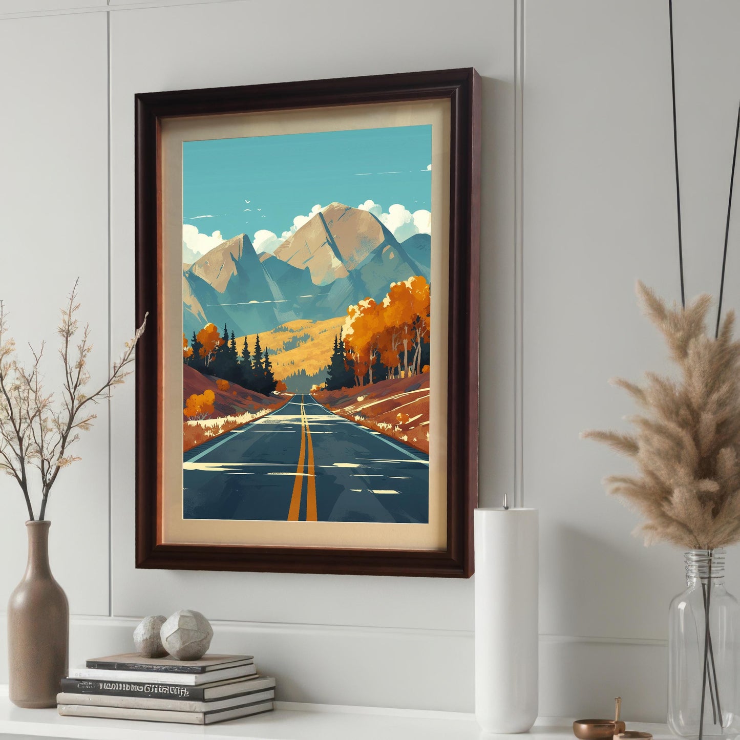 Close-up of a coffee-colored wood frame with a cream mount featuring landscape art, displayed on a white shelf alongside books, candles, and decorative pampas grass.