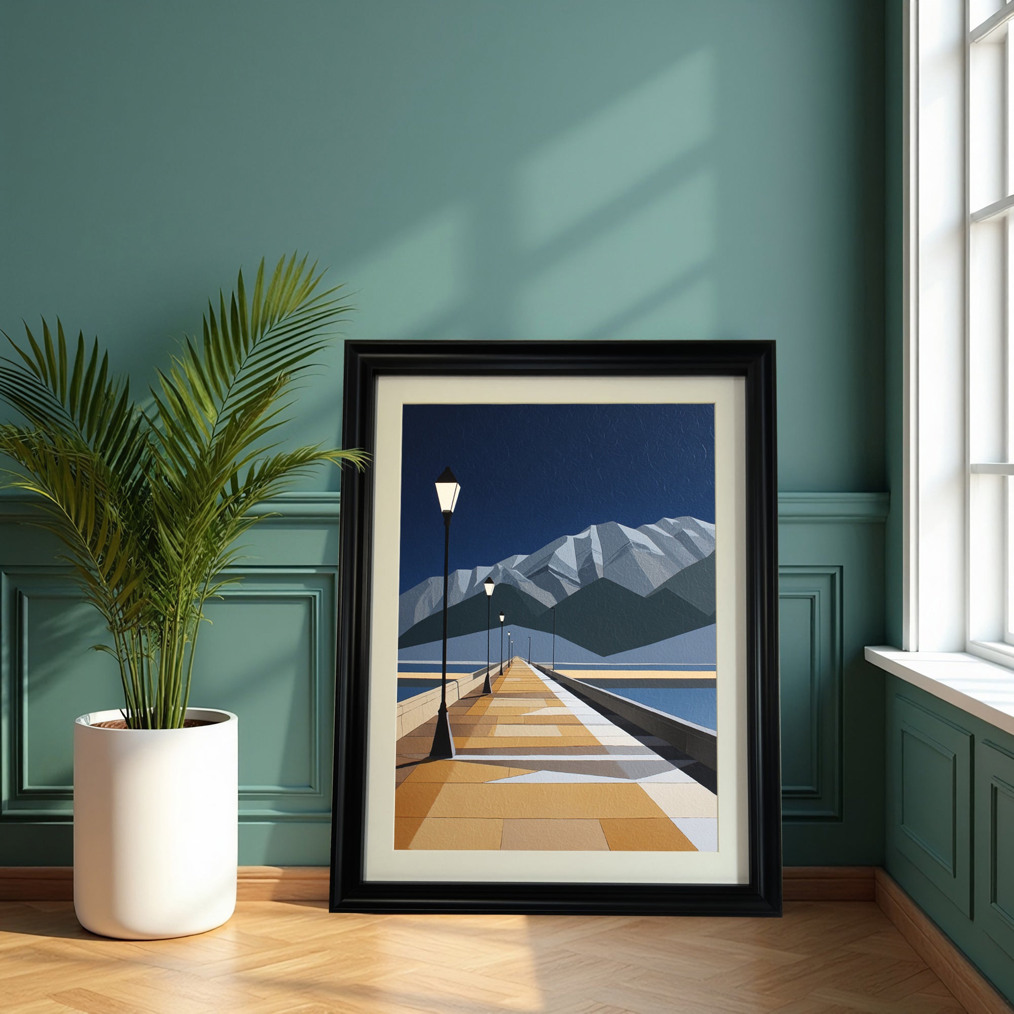 Geometric art print of a pier leading into the distance toward mountains, in a thick black frame, leaning on a wooden floor against a dark teal paneled wall next to a potted palm plant.