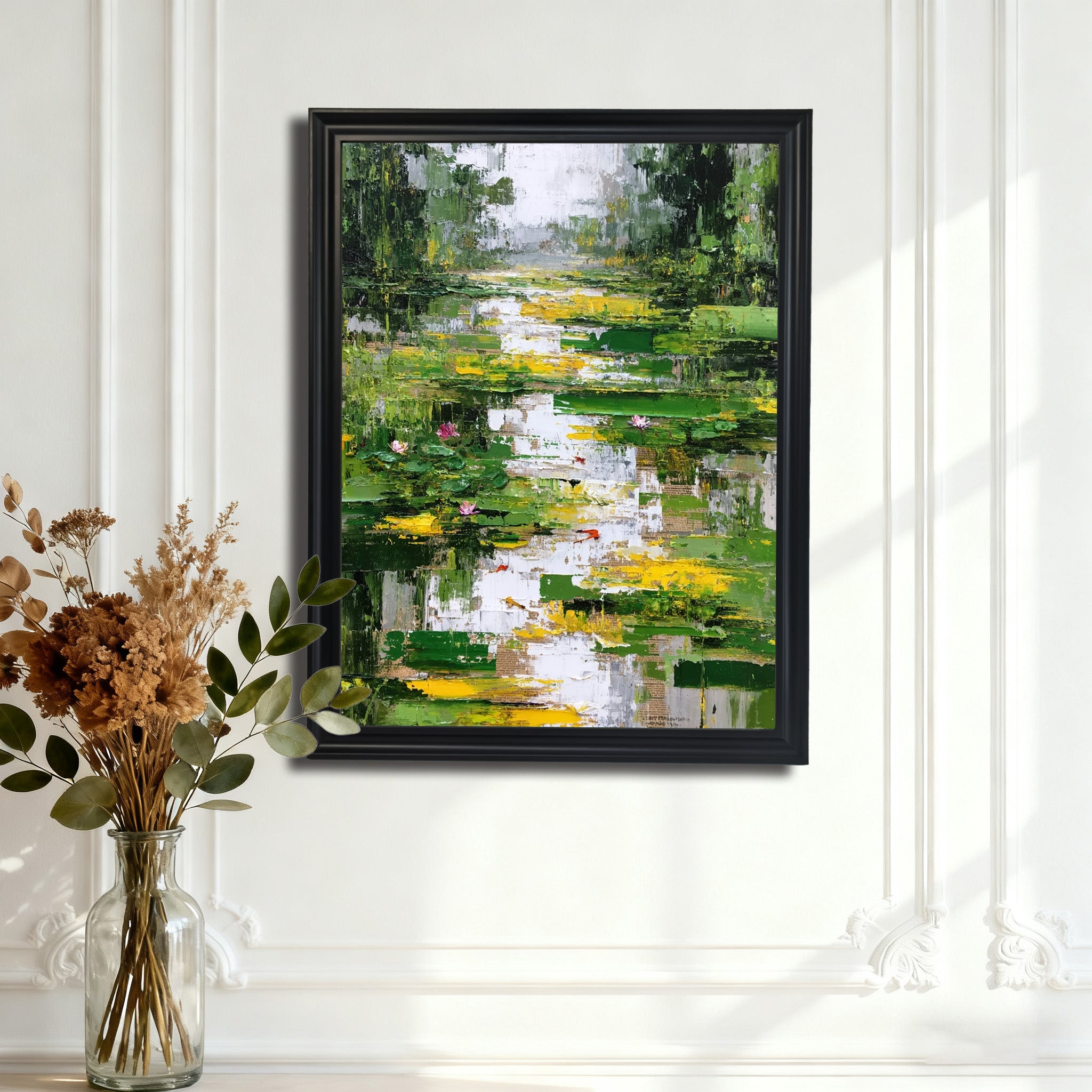 Abstract lily pond painting in a black frame, hanging on a white wall with decorative trim, with a glass vase of dried florals in the foreground.