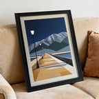 Geometric pier and mountain art print in a black frame, angled while resting on a tan fabric sofa with a rust-colored pillow.
