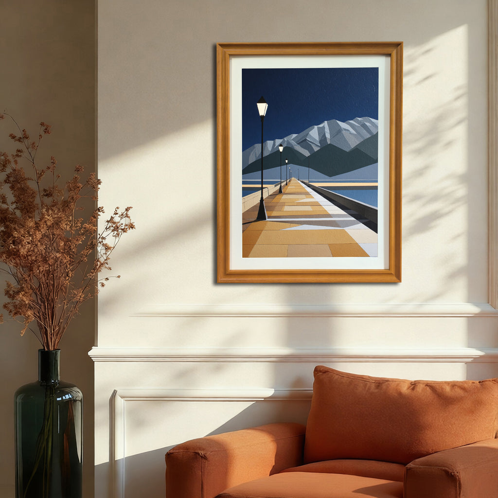 Geometric landscape art print depicting a pier, lake, and mountains, in a gold-colored wood frame, hanging on a beige wall above an orange armchair.