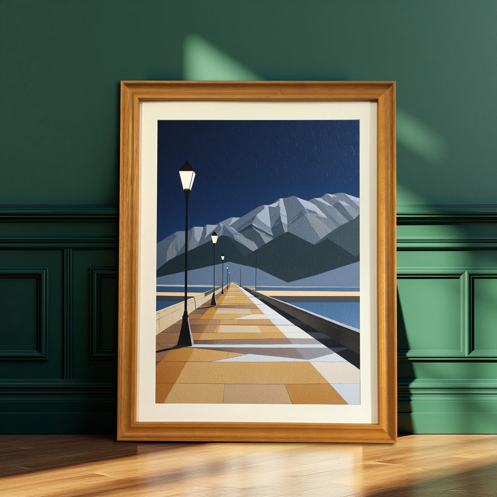 Geometric art print of a pier leading into the distance toward mountains, in a thick black frame, leaning on a wooden floor against a dark teal paneled wall next to a potted palm plant.