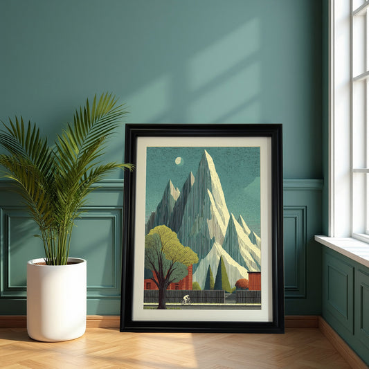 Large, black-framed art print of the mountain and cyclist scene resting on the floor next to a potted palm, against a teal green paneled wall near a bright window.