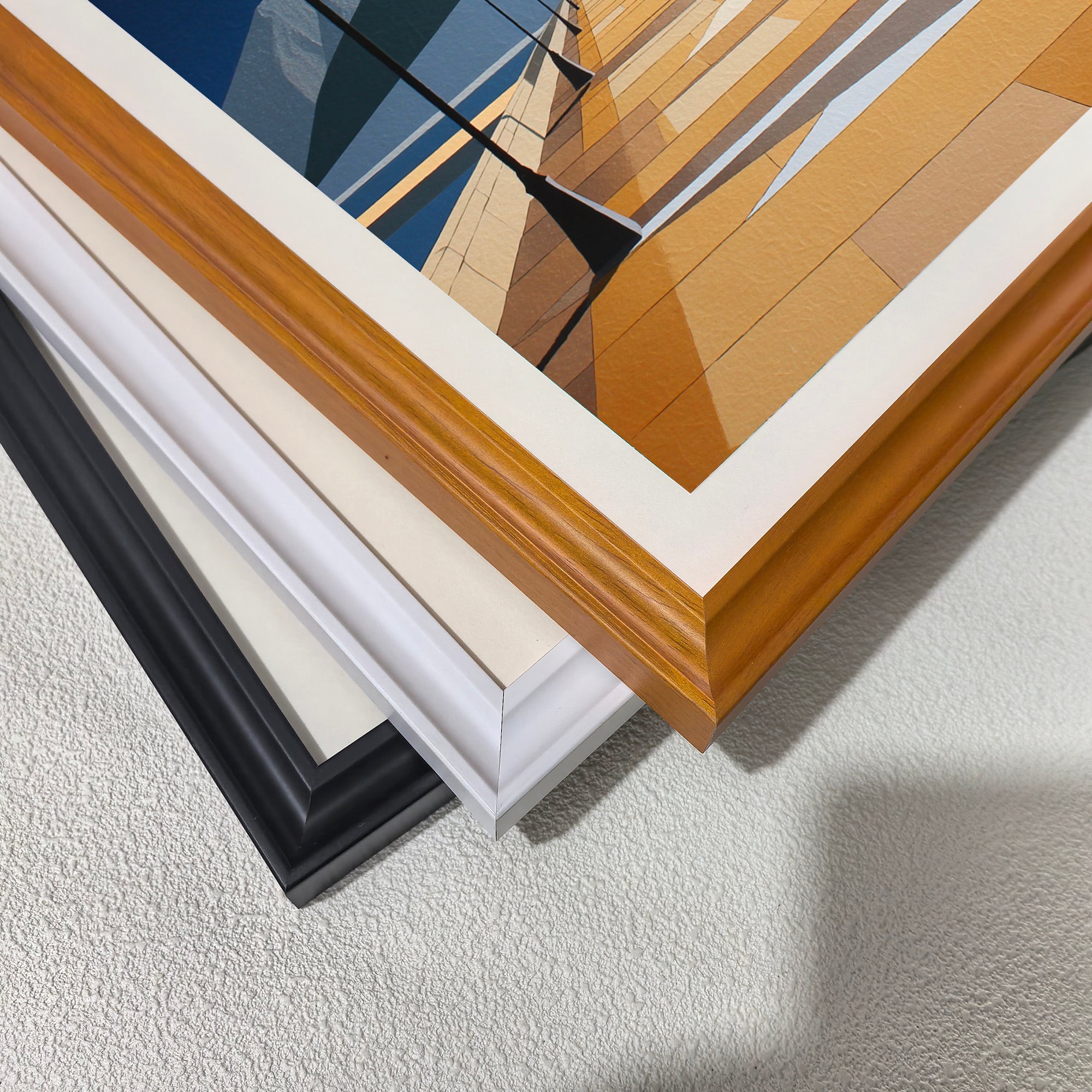 Close-up corner detail of the geometric pier and mountain artwork showing three stacked frame options: natural wood, white, orange, and black.