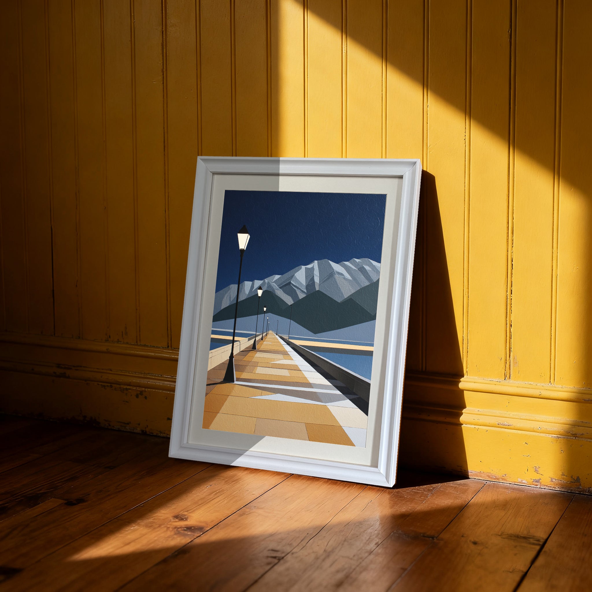 Geometric pier and mountain print in a white frame, leaning on a wooden floor against a bright yellow beadboard wall, illuminated by strong window light."