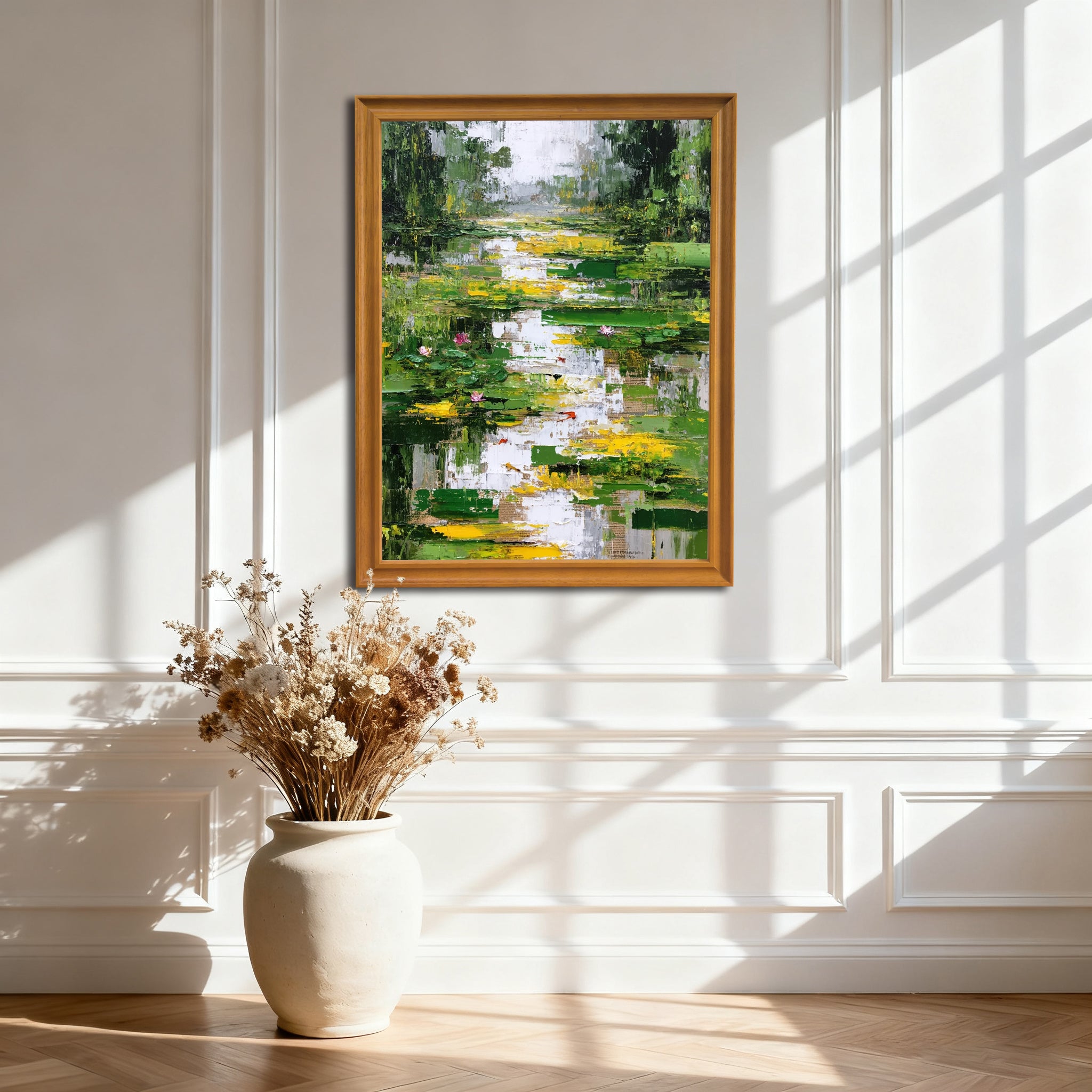 Abstract lily pond painting in a gold-colored wooden frame, hanging on an elegant white wall with decorative wainscoting and natural light creating strong window pane shadows, above a large white vase with dried flowers.