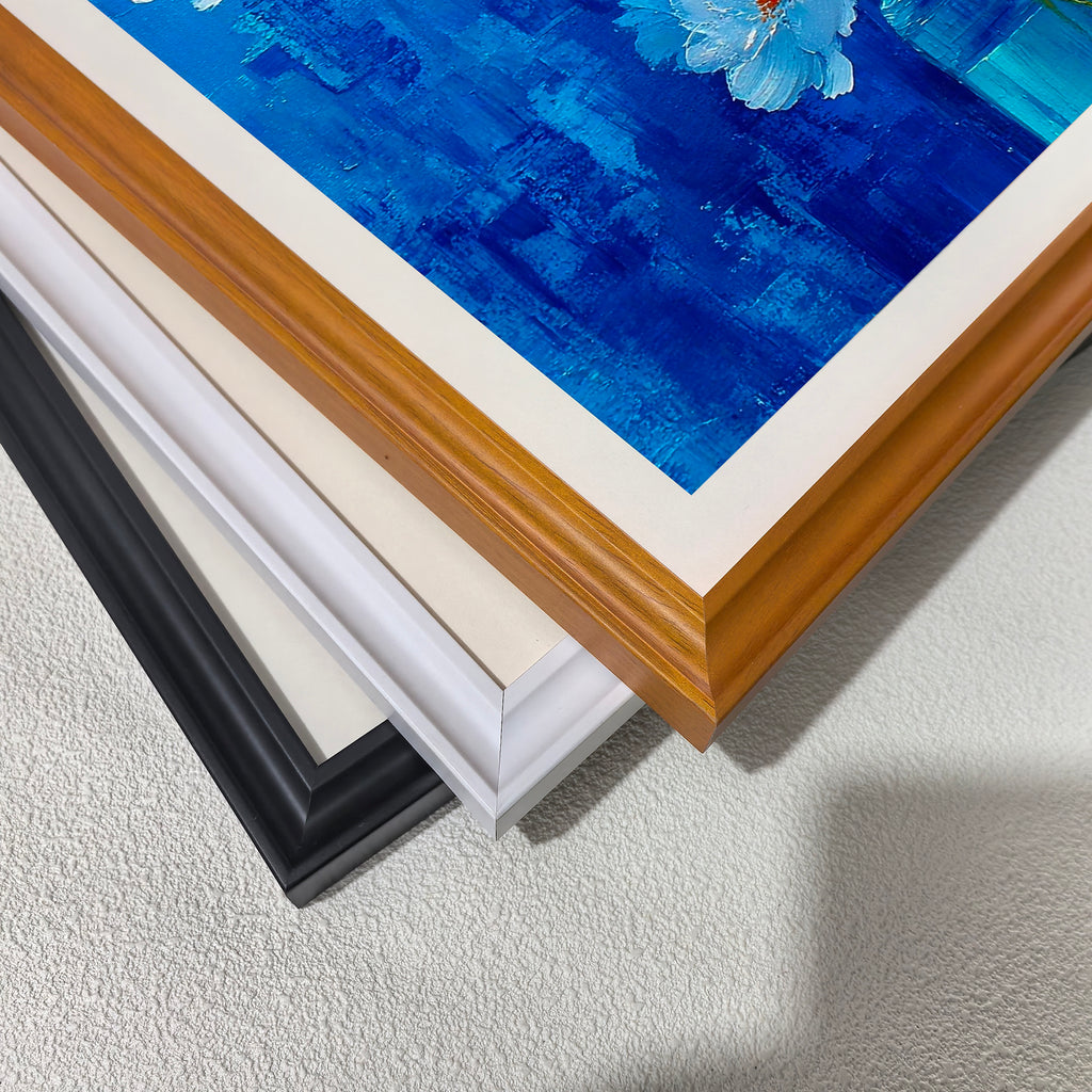 A close-up, stacked view of the corners of three different wooden print frames: black, white, off-white, and light brown (wood grain), placed over a section of the painting's blue background.