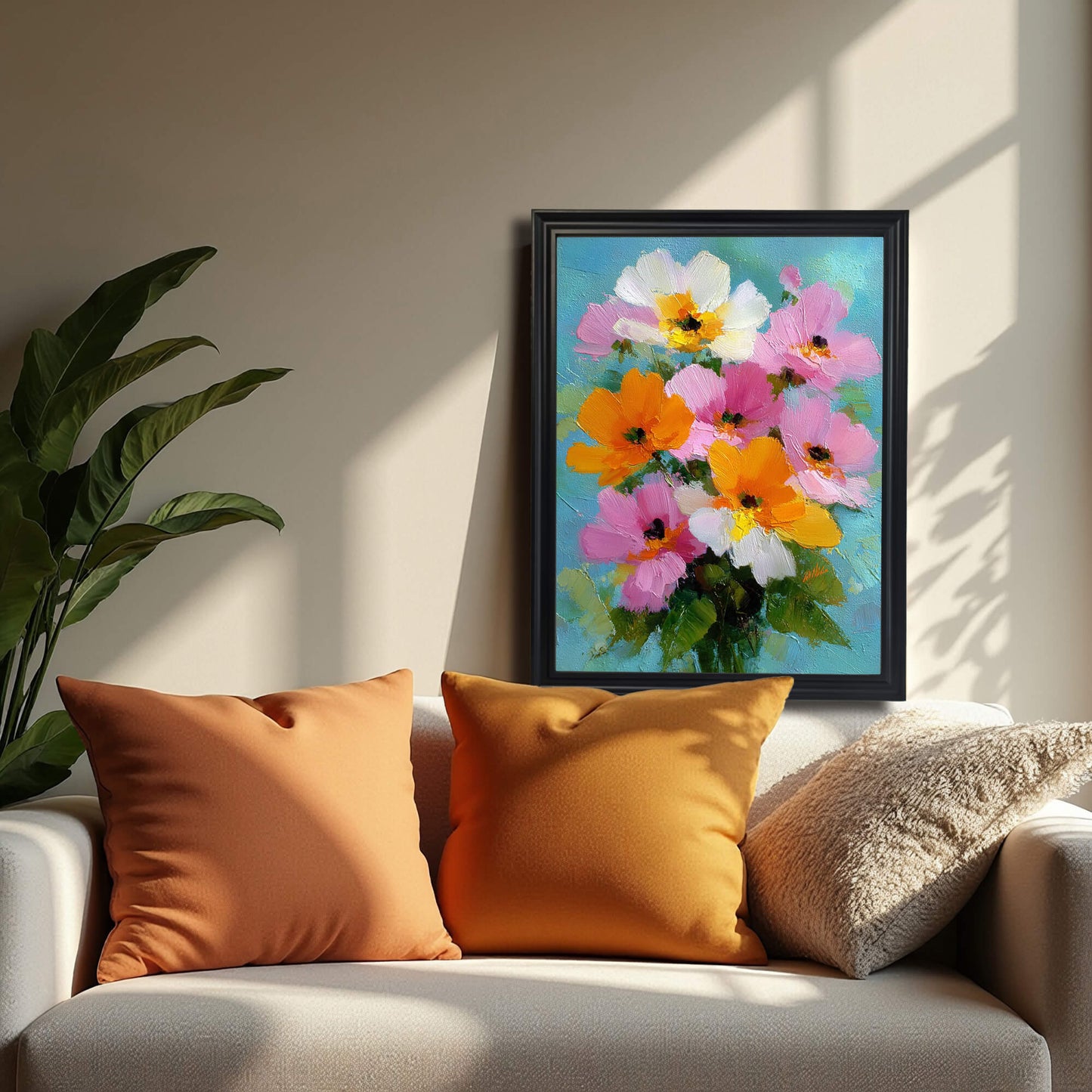 A black-framed version of the floral painting hanging on a neutral wall above a sofa with two orange pillows and one beige textured pillow, cast in soft afternoon shadows.