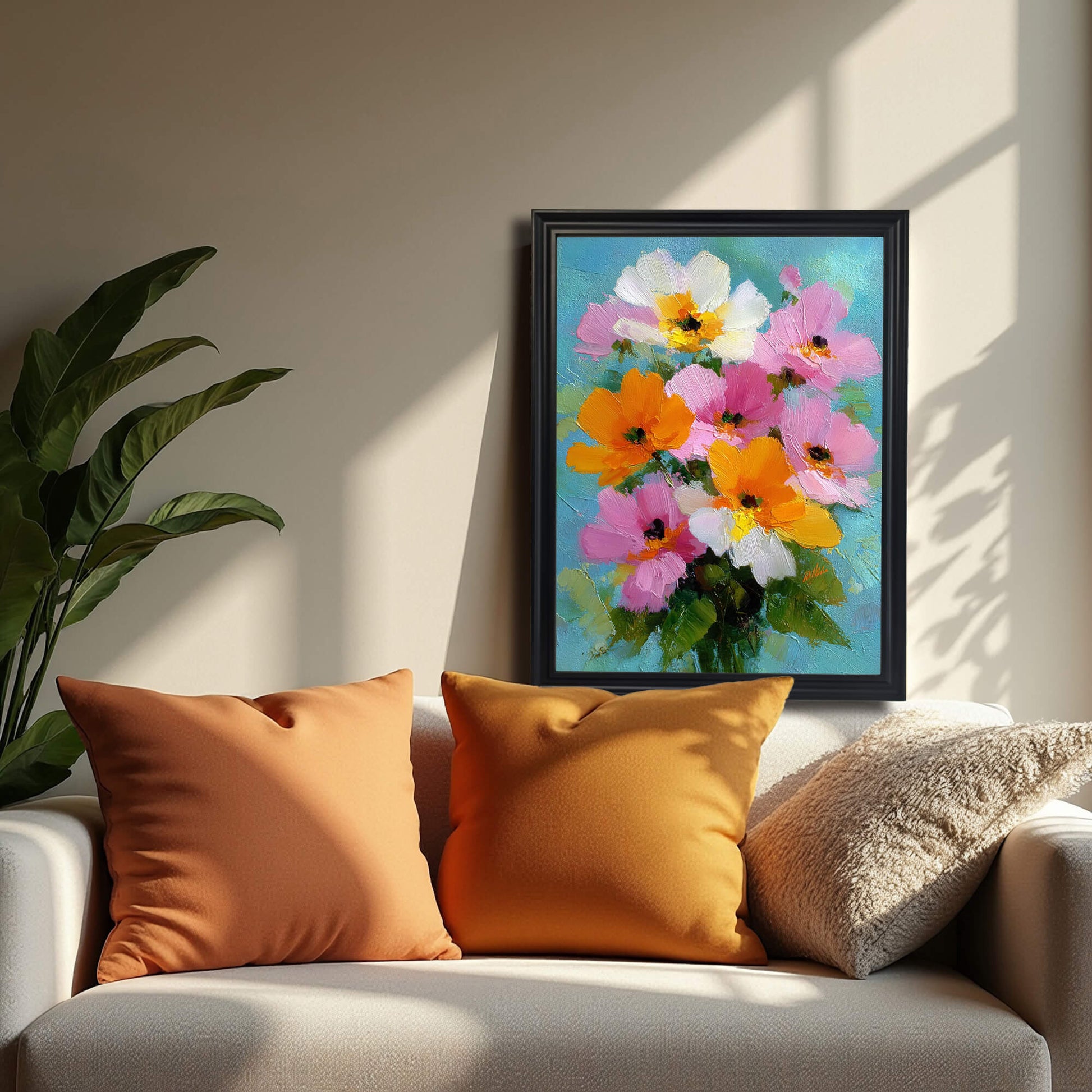 A black-framed version of the floral painting hanging on a neutral wall above a sofa with two orange pillows and one beige textured pillow, cast in soft afternoon shadows.