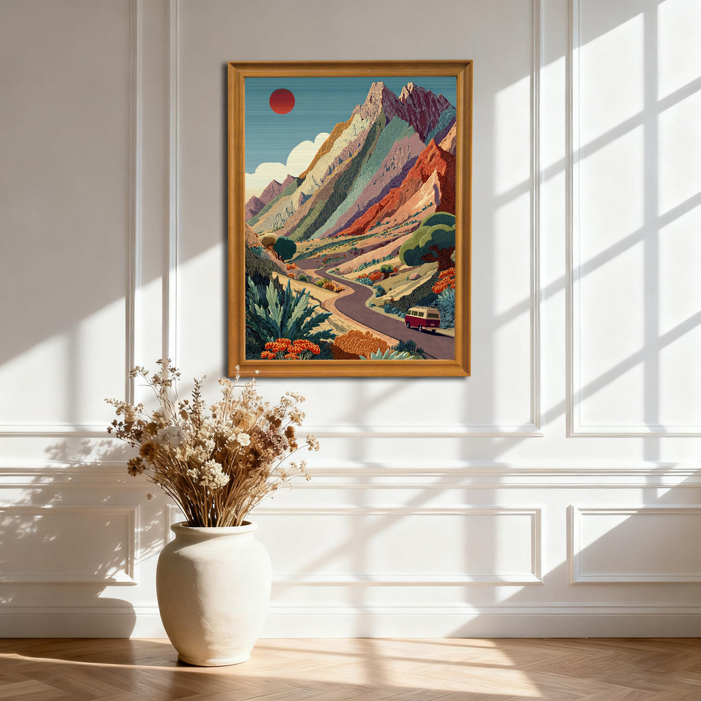 Natural wood-framed art print of the colorful mountain road trip scene, hanging on a white paneled wall. Sunlight casts dramatic geometric shadows.