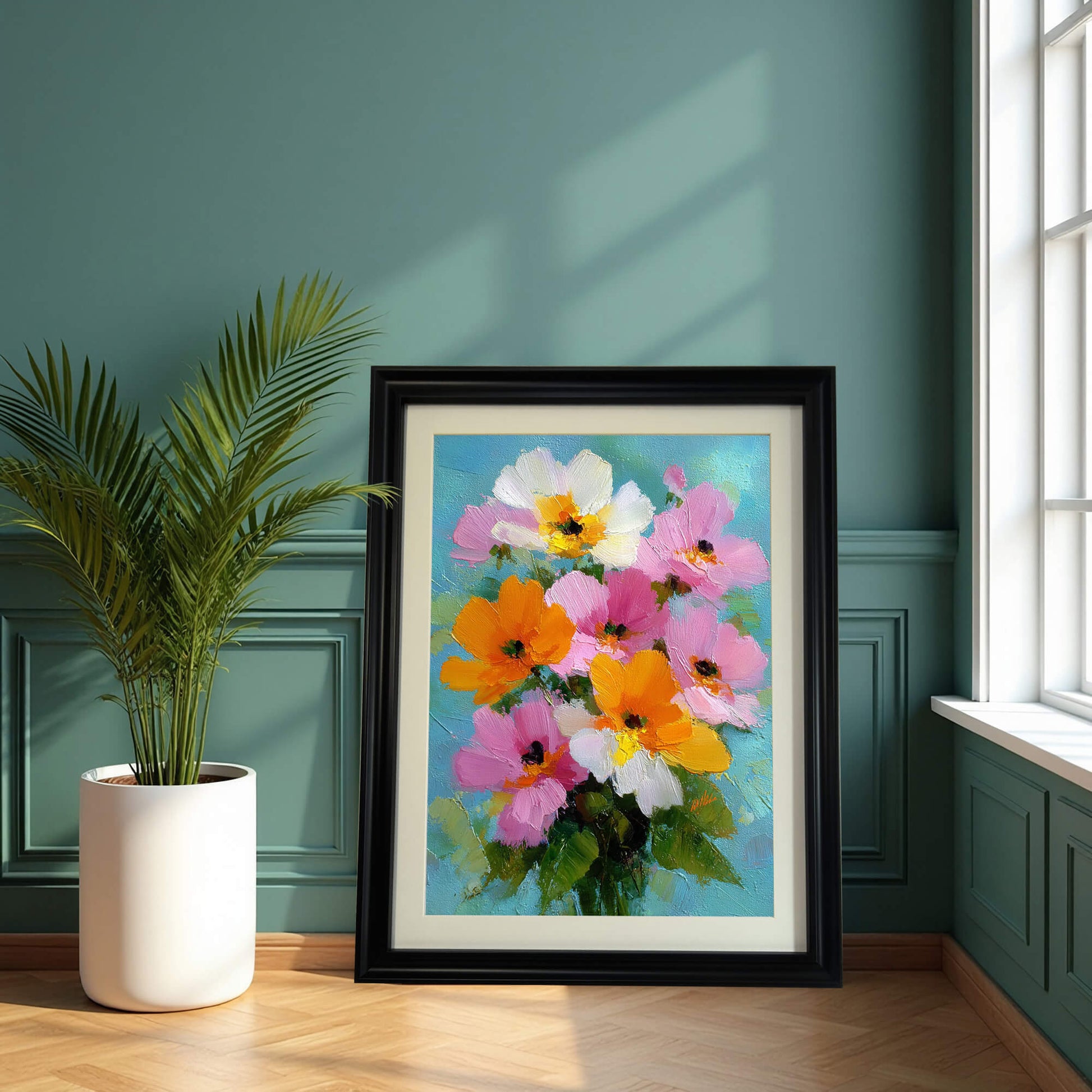 A large black-framed floral painting leaning on a wooden floor against a dark teal wall with classic paneling, next to a potted palm plant.