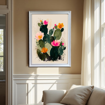 The abstract blooming cactus art print, framed in a contemporary white frame, is hung in a living room with beige walls and large windows, showcasing the artwork's bright colors over a white sofa.