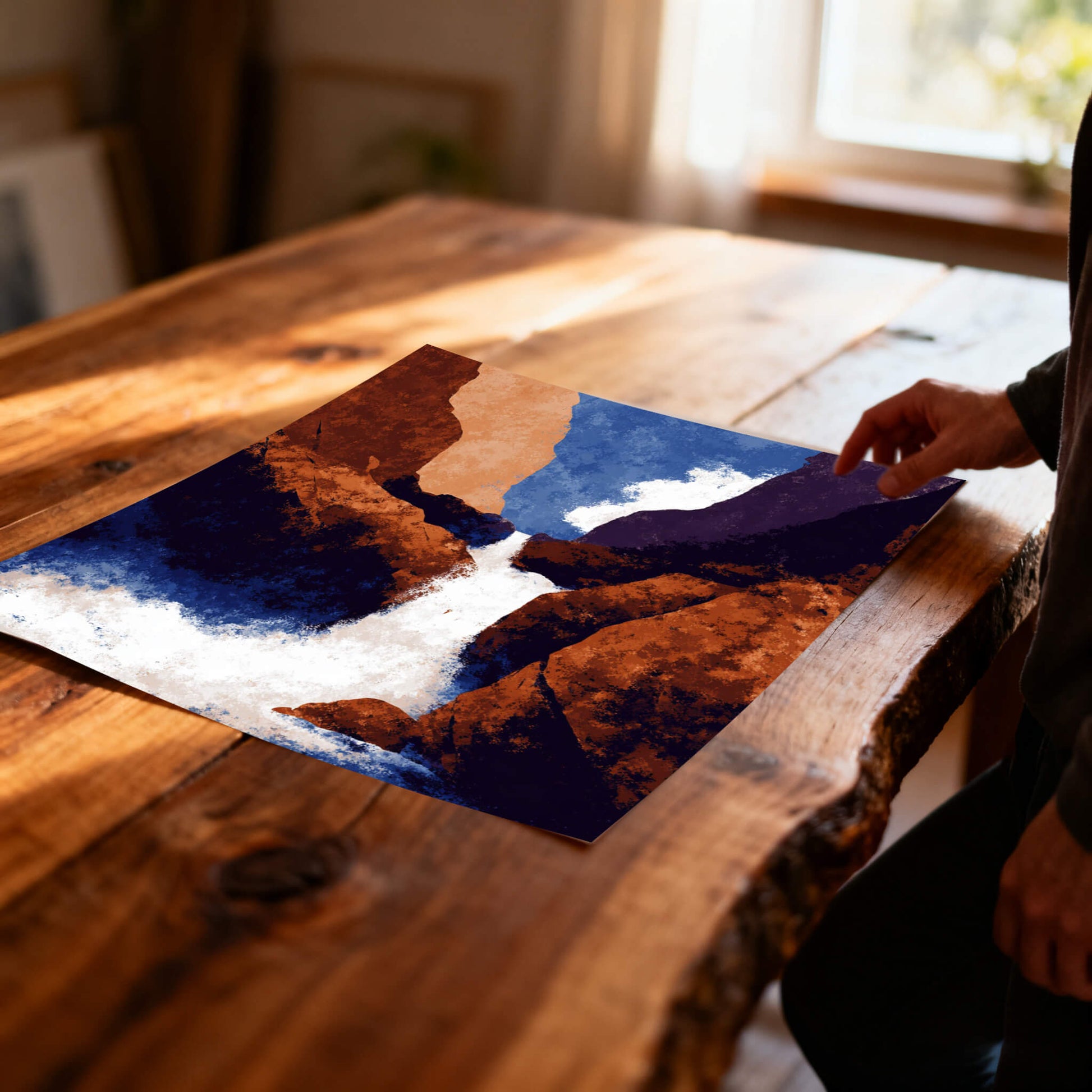 Unframed abstract waterfall art print with strong blue and orange colors, lying on a rustic, live-edge wooden table in soft sunlight.