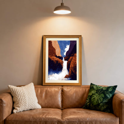 Framed abstract waterfall print in a light wood (natural) frame, hanging over a brown leather couch with textured and monstera-leaf print pillows.