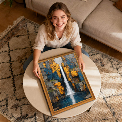 A smiling woman sits on a rug, holding a portrait-orientation abstract waterfall art print in a golden wood frame on a coffee table.