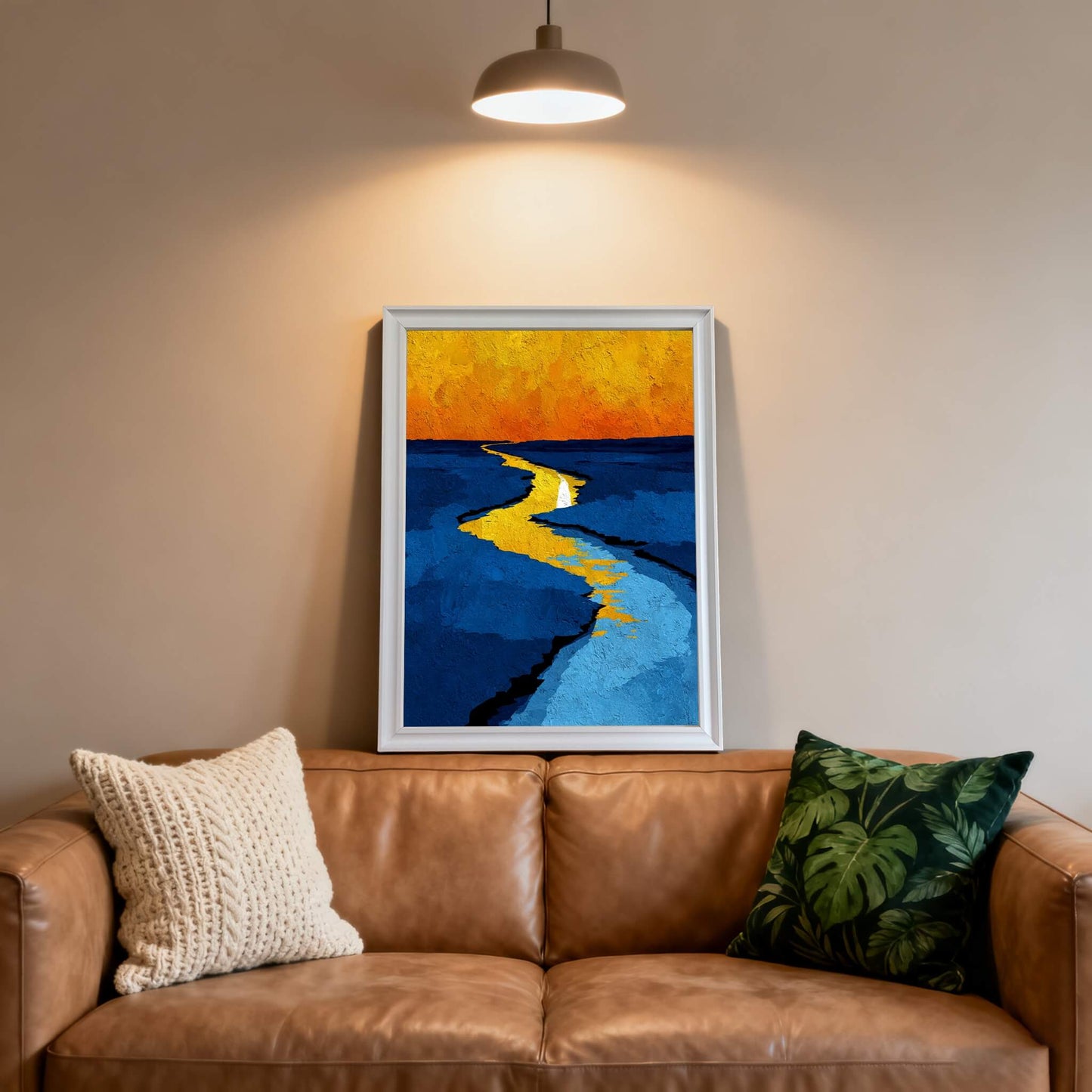 Abstract print of the bright yellow path on blue, framed in white, hanging over a brown leather couch with textured and tropical print pillows.
