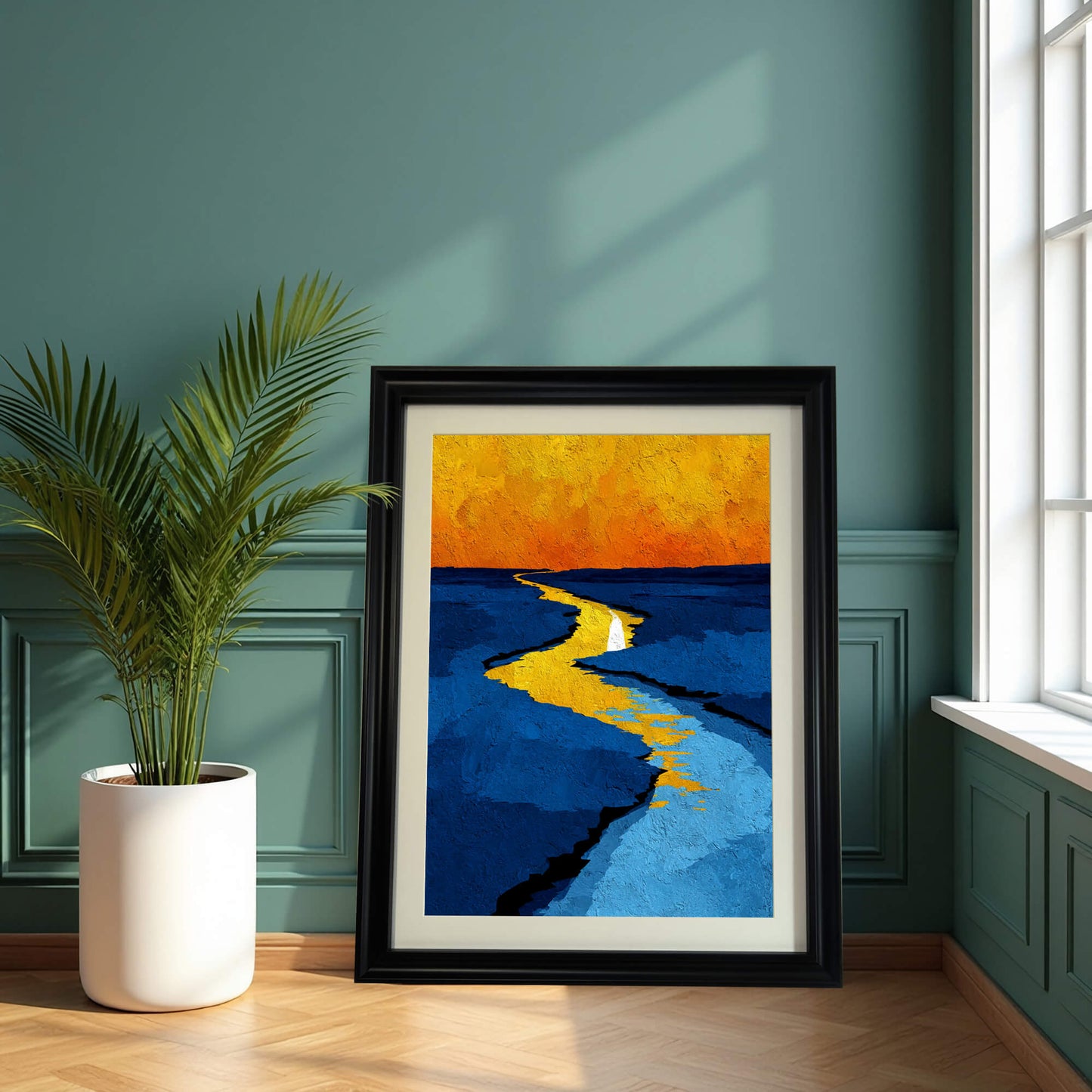 Abstract print of the yellow river landscape in a black frame, leaning on a wooden floor against a dark green paneled wall next to a house plant.