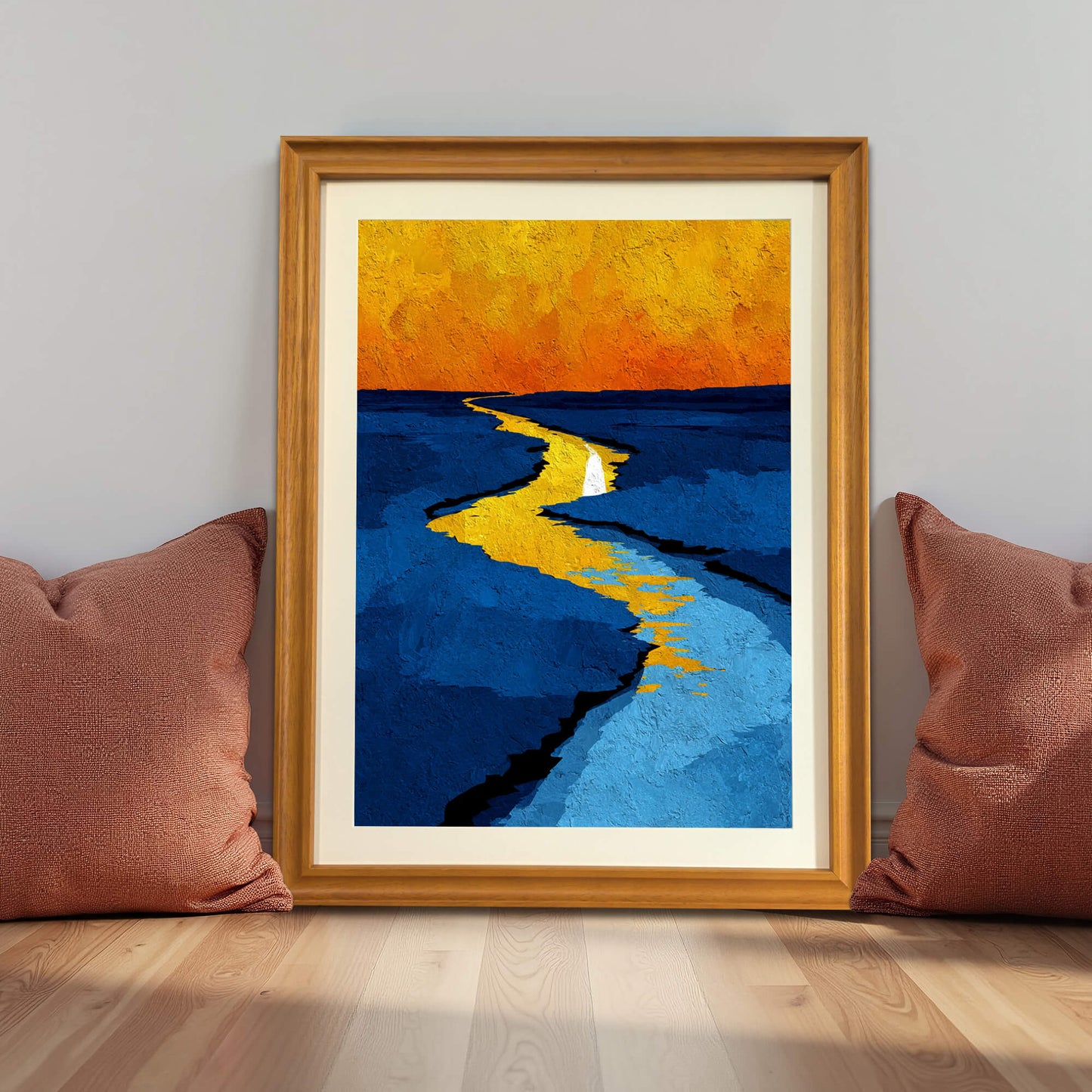 Abstract print of the yellow path through blue fields, framed in light wood (natural), leaning against a gray wall between two rust-colored pillows.