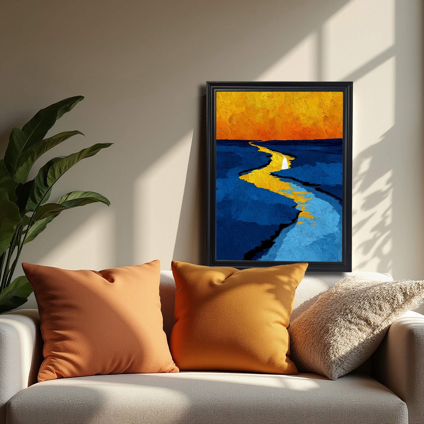 Abstract print of a yellow path or river against blue tones and an orange sky, framed in black, resting on a white sofa next to orange pillows.
