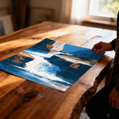 Overhead shot of a hand touching an unframed art print with a blue and orange waterfall abstract on a rustic, live-edge wood table, with natural light pouring in from a window.