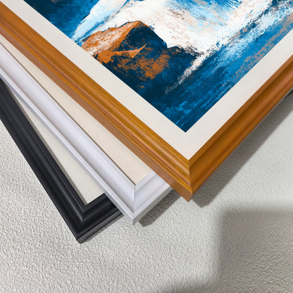 Close-up stack of three wood picture frames—black, white, and natural light brown wood—displaying a painting with abstract blue, white, and orange brushstrokes, suggesting different framing options.
