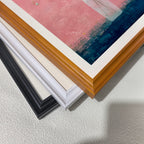 Close-up view of three stacked wood picture frame corners in black, white, and natural brown, showing the art print inside which features vibrant pink and dark blue colors.