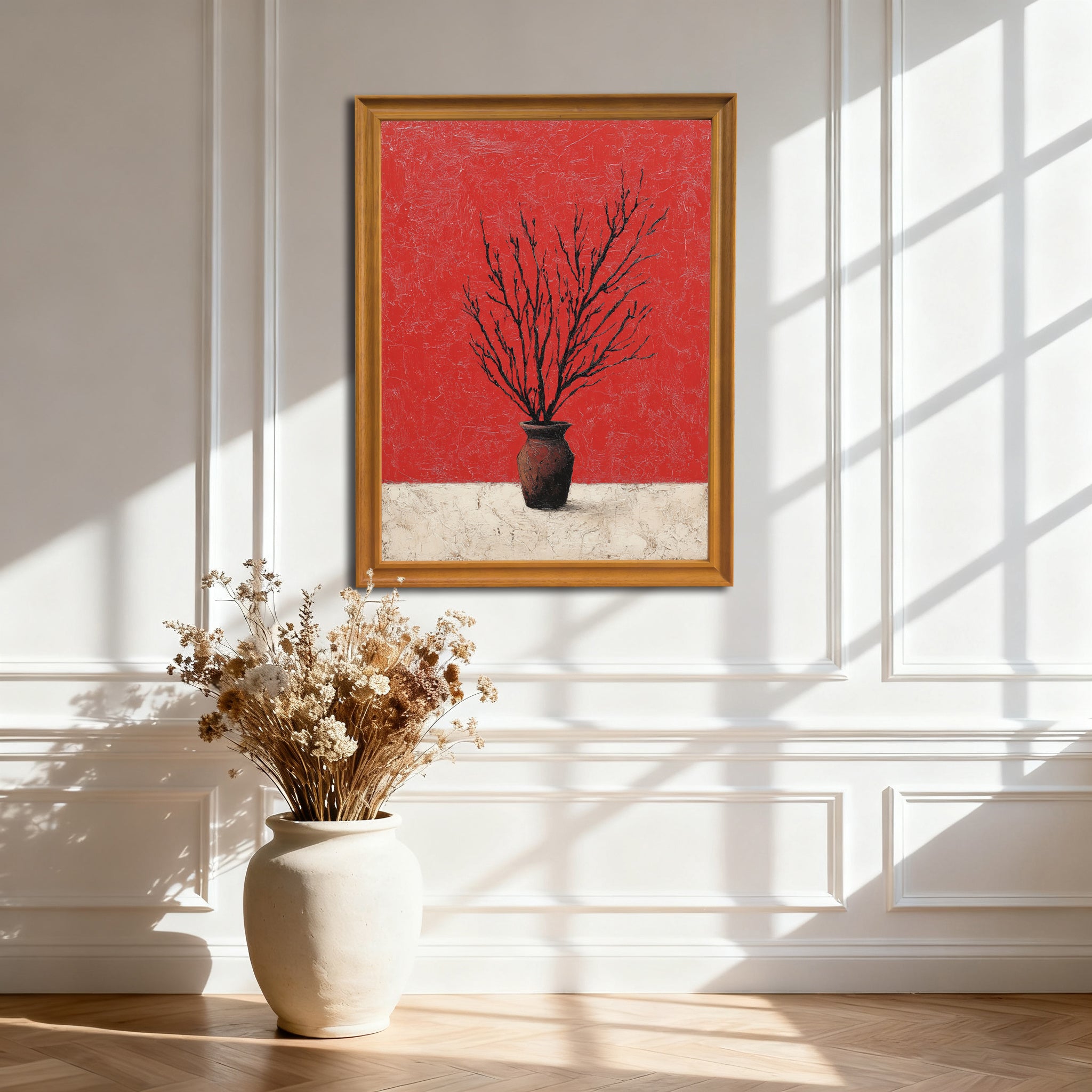 Gold-colored wood framed art print of branches in a vase against a textured red and white background, hanging on a white wainscoting wall with natural window light and shadows.
