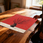 Unframed art print of black branches in a vase on a red and textured white background, lying on a rustic wooden table with a person's hand nearby.