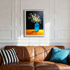 A white-framed art print centered above a brown leather sofa with striped and blue pillows. The white paneled wall provides a bright setting for the high-contrast floral still life artwork.